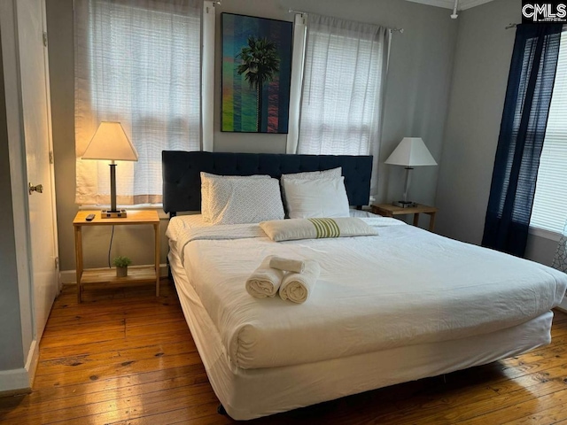 bedroom featuring multiple windows, baseboards, and wood finished floors