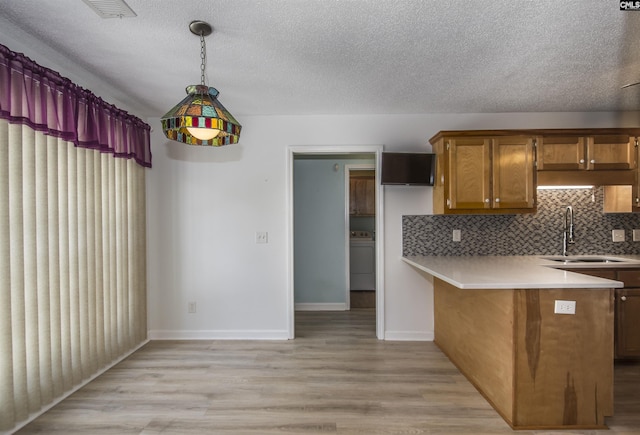 kitchen with pendant lighting, light countertops, brown cabinetry, a sink, and washer / dryer