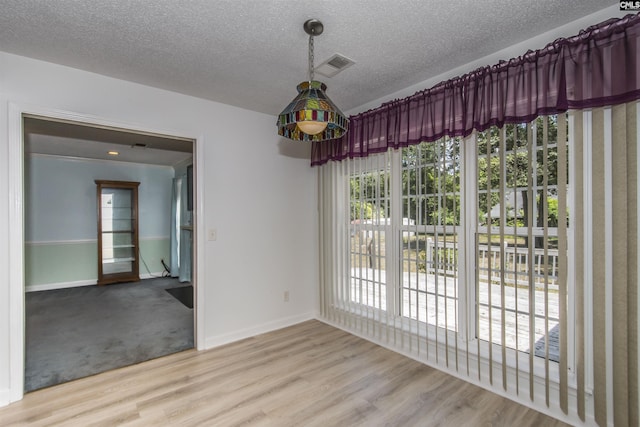 spare room with a textured ceiling, wood finished floors, visible vents, and baseboards