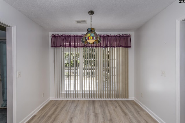 unfurnished dining area featuring visible vents, a textured ceiling, baseboards, and wood finished floors