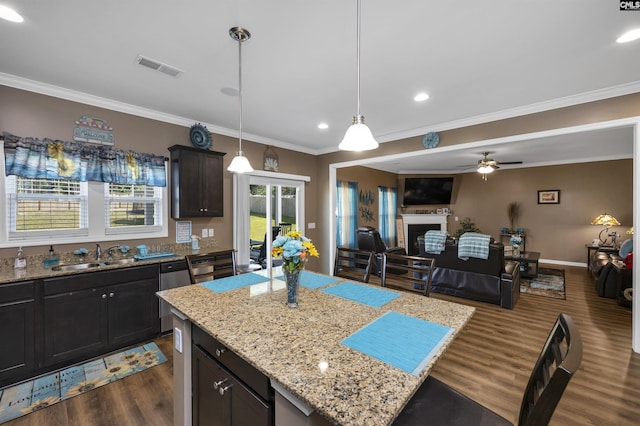 kitchen with a fireplace, a kitchen island, a sink, open floor plan, and hanging light fixtures