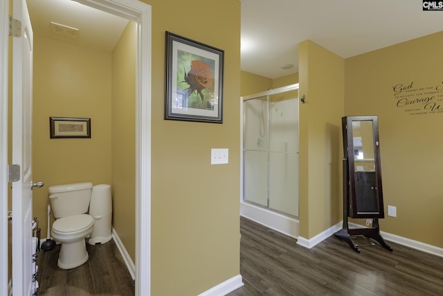 full bath featuring toilet, a stall shower, baseboards, and wood finished floors