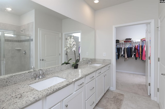 bathroom featuring a spacious closet, double vanity, a stall shower, and a sink