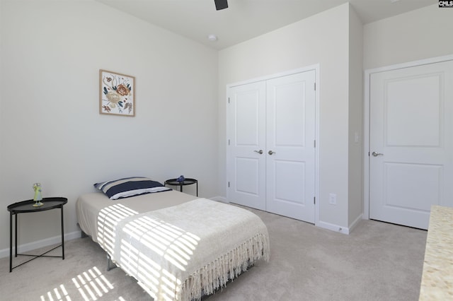 bedroom with a closet, light colored carpet, ceiling fan, and baseboards