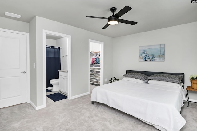 bedroom with a walk in closet, a closet, light colored carpet, ensuite bathroom, and baseboards