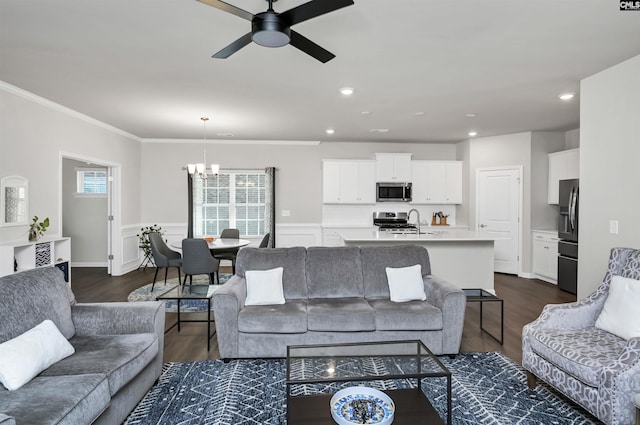 living area with recessed lighting, ceiling fan with notable chandelier, a wainscoted wall, dark wood-style floors, and crown molding