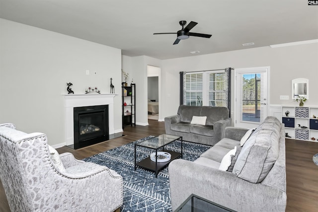 living area with a glass covered fireplace, dark wood-style flooring, visible vents, and ceiling fan