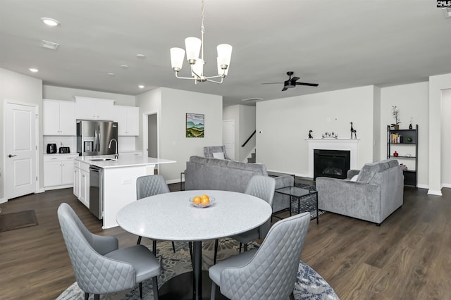 dining area featuring recessed lighting, ceiling fan with notable chandelier, dark wood-style flooring, stairs, and a glass covered fireplace