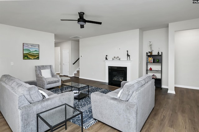 living area featuring visible vents, dark wood-type flooring, a glass covered fireplace, baseboards, and stairs