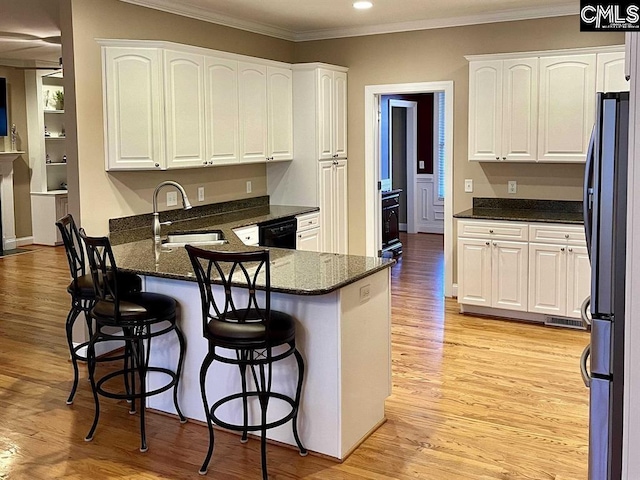 kitchen featuring a breakfast bar area, a sink, white cabinets, black dishwasher, and dark stone countertops