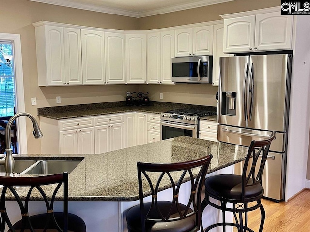 kitchen featuring dark stone counters, light wood-style flooring, appliances with stainless steel finishes, crown molding, and white cabinetry