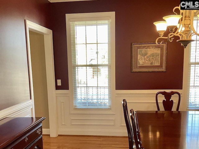 dining space with an inviting chandelier, a decorative wall, light wood finished floors, and wainscoting