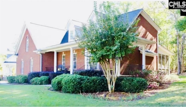 view of side of home featuring covered porch, brick siding, and a lawn