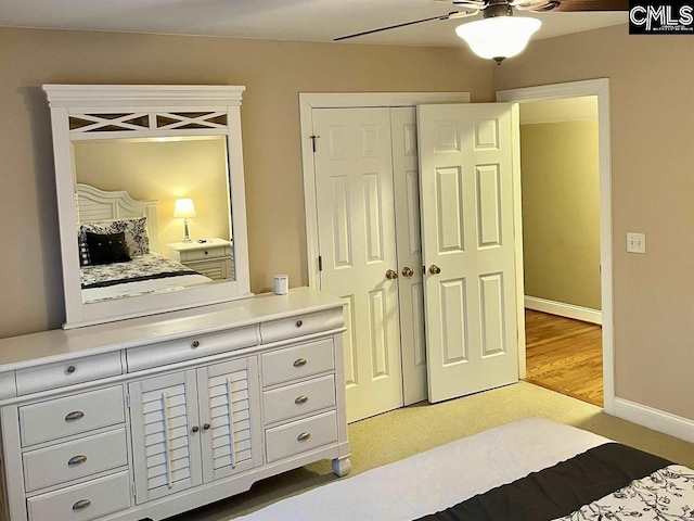 bedroom with a closet, light colored carpet, a ceiling fan, and baseboards