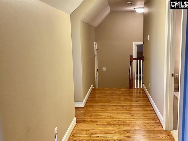 hallway featuring light wood-style flooring, baseboards, vaulted ceiling, and an upstairs landing