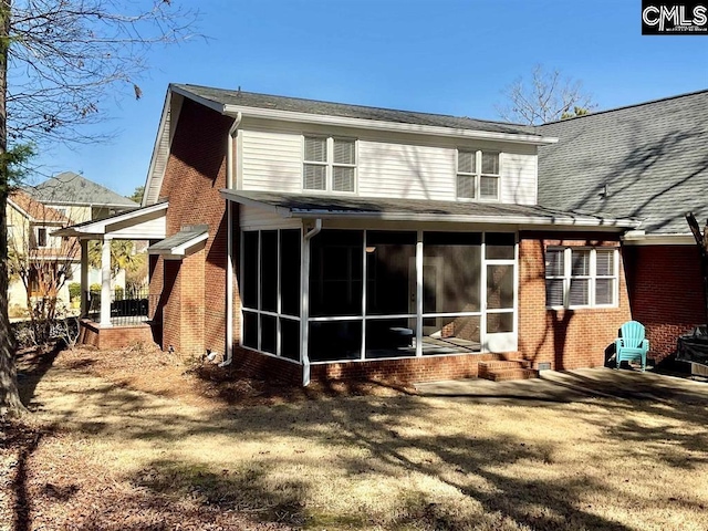 rear view of property with a sunroom, a lawn, and brick siding