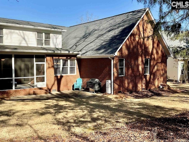 rear view of property featuring a sunroom, brick siding, and a lawn