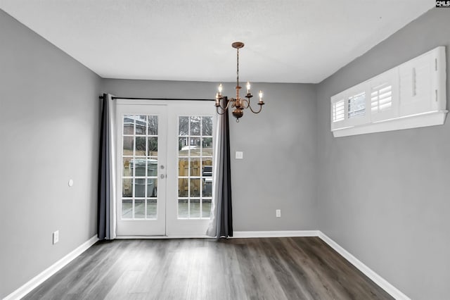 unfurnished dining area with french doors, a notable chandelier, dark wood finished floors, and baseboards