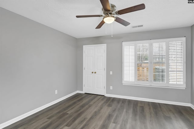 spare room featuring baseboards, visible vents, dark wood finished floors, a ceiling fan, and a textured ceiling