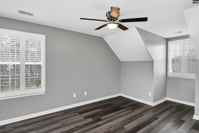 additional living space featuring dark wood-style floors, baseboards, visible vents, and vaulted ceiling