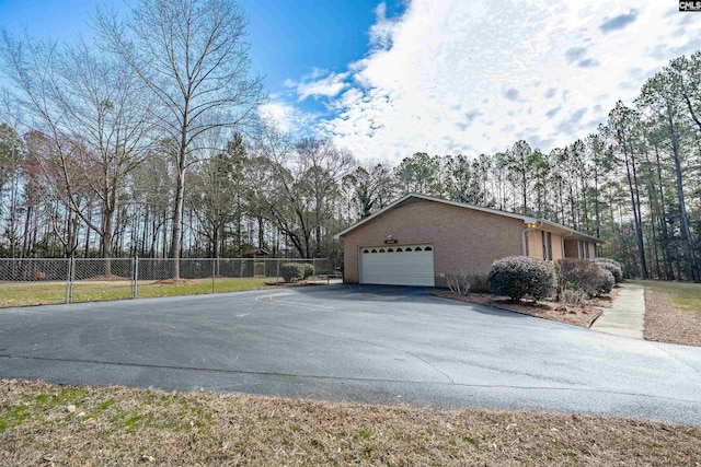 view of side of home featuring driveway, brick siding, an attached garage, and fence