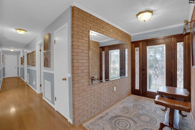 foyer featuring a textured ceiling, brick wall, visible vents, light wood-style floors, and crown molding