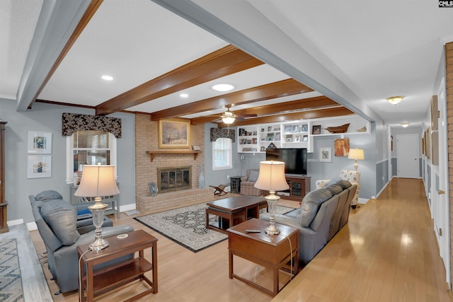 living room with baseboards, a ceiling fan, light wood-type flooring, a fireplace, and beam ceiling