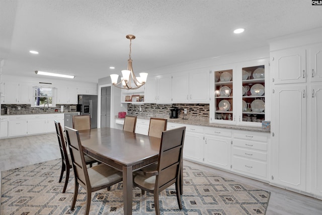 dining room with a textured ceiling, recessed lighting, light wood-type flooring, and a notable chandelier