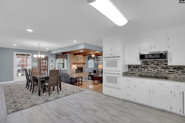 kitchen with double oven, light stone counters, black electric cooktop, a large fireplace, and white cabinets