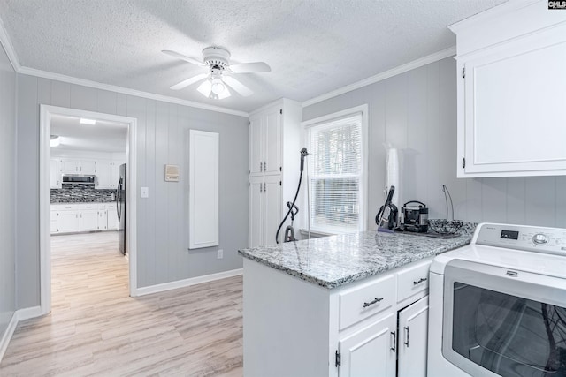 kitchen featuring washer / dryer, white cabinets, stainless steel microwave, crown molding, and light wood-style floors