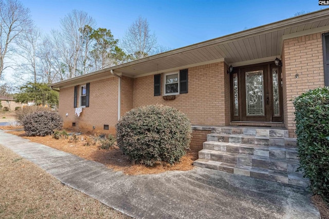 view of exterior entry with crawl space and brick siding