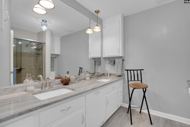 full bath featuring double vanity, wood finished floors, a sink, and a shower stall