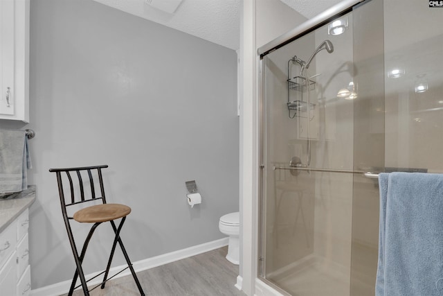 full bath featuring toilet, a textured ceiling, a shower stall, wood finished floors, and baseboards