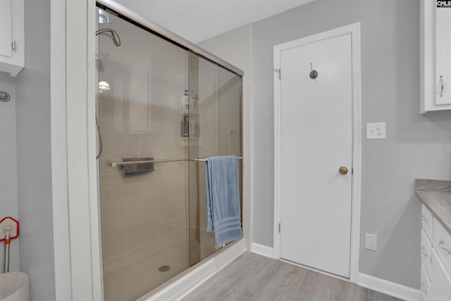 bathroom featuring a stall shower, vanity, a textured ceiling, wood finished floors, and baseboards