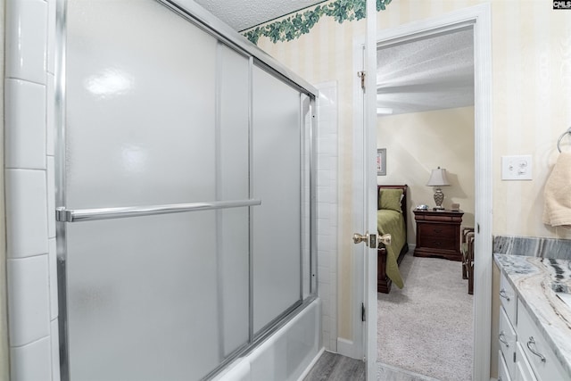 ensuite bathroom featuring shower / bath combination with glass door, connected bathroom, a textured ceiling, and vanity