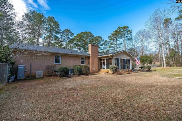 rear view of house featuring a sunroom, a chimney, brick siding, and a yard