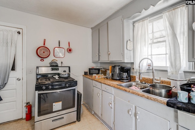 kitchen with light countertops, gray cabinets, gas stove, and a sink