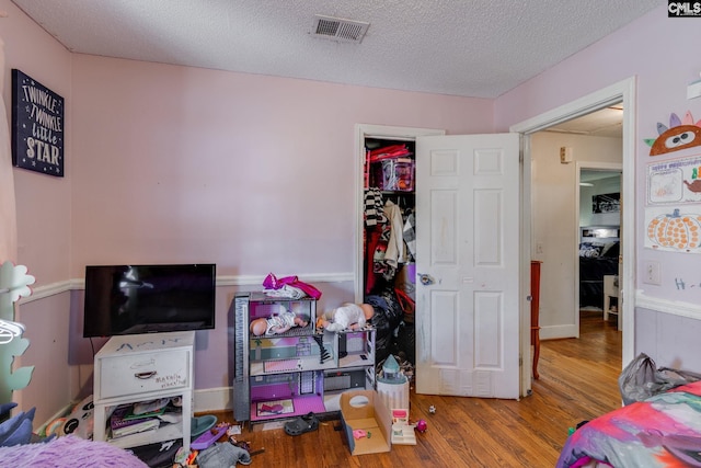 bedroom with visible vents, a textured ceiling, and wood finished floors