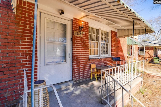 view of exterior entry featuring brick siding and a porch