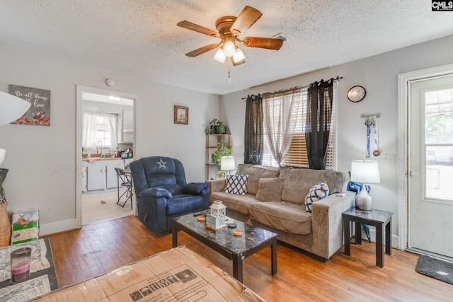 living area featuring baseboards, ceiling fan, a textured ceiling, and light wood finished floors