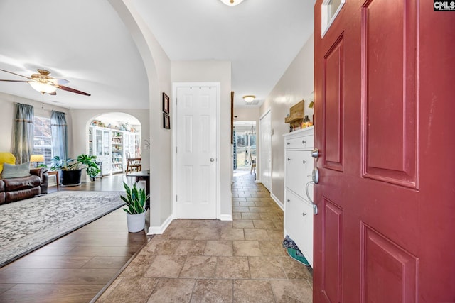 foyer entrance with ceiling fan, arched walkways, and baseboards