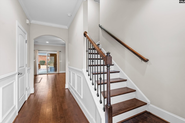 staircase featuring baseboards, crown molding, arched walkways, and wood finished floors