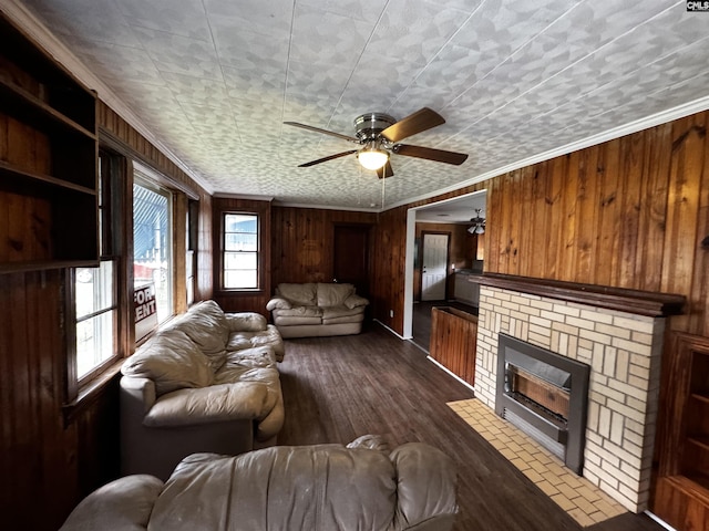 living area with a ceiling fan, dark wood-style flooring, crown molding, wood walls, and a fireplace