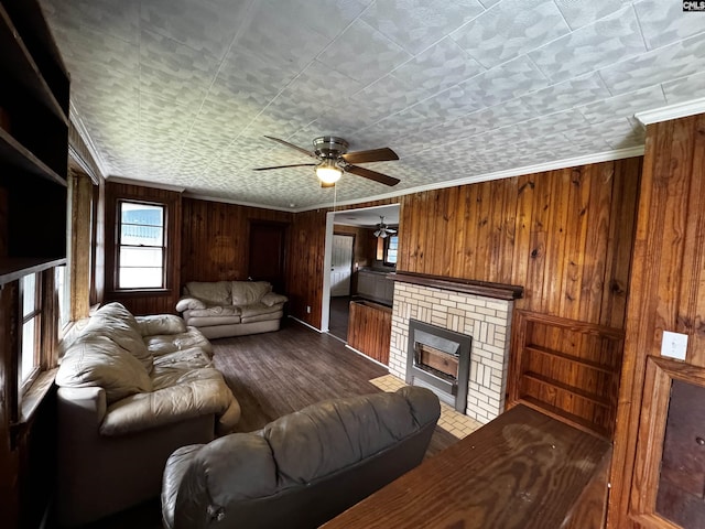 living area with a ceiling fan, wood finished floors, crown molding, wood walls, and a brick fireplace