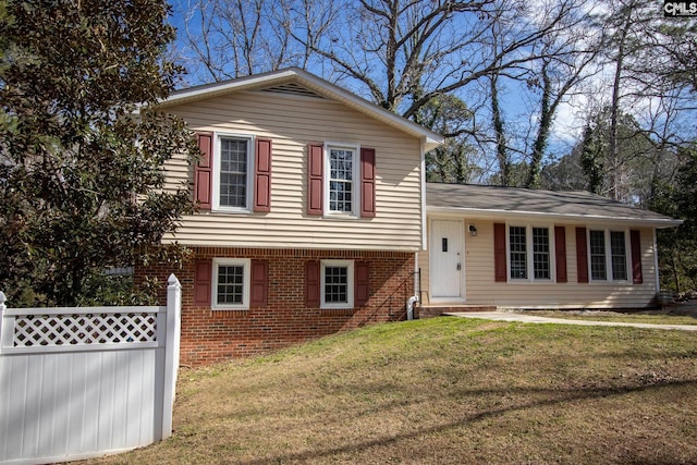 tri-level home with a front yard, fence, and brick siding