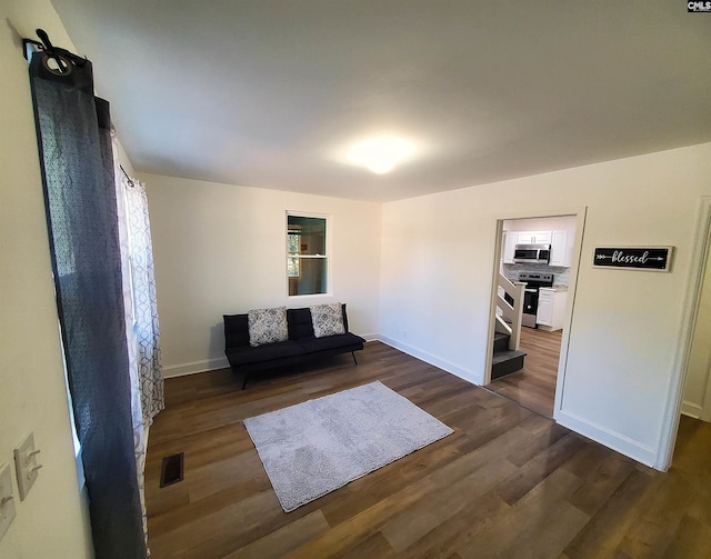 unfurnished room featuring stairway, dark wood-style flooring, visible vents, and baseboards