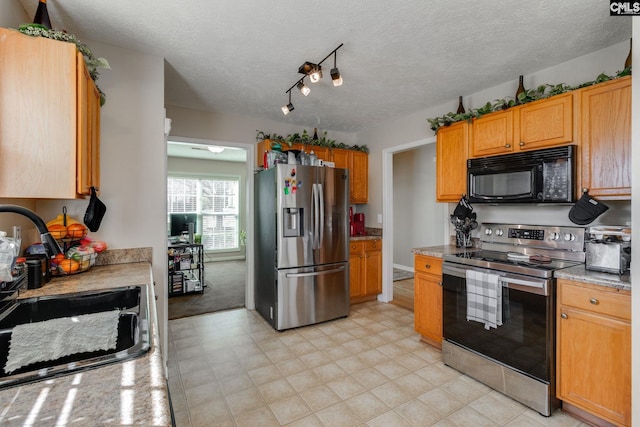 kitchen with a textured ceiling, stainless steel appliances, a sink, light stone countertops, and rail lighting