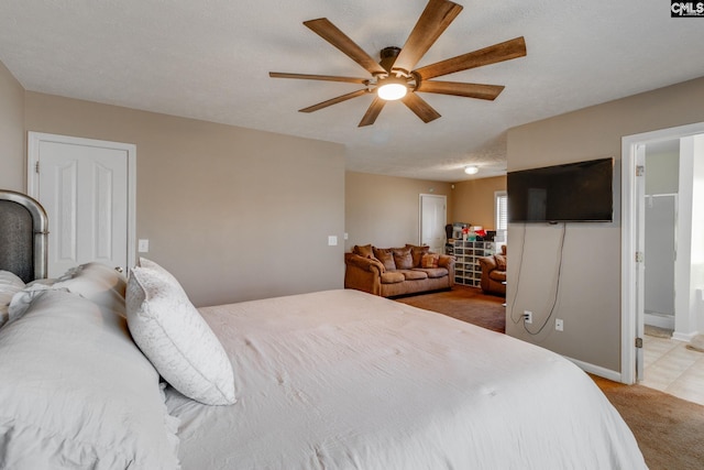 bedroom featuring baseboards, light colored carpet, ensuite bath, ceiling fan, and a textured ceiling