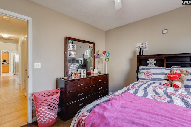 bedroom featuring freestanding refrigerator, ceiling fan, and a textured ceiling