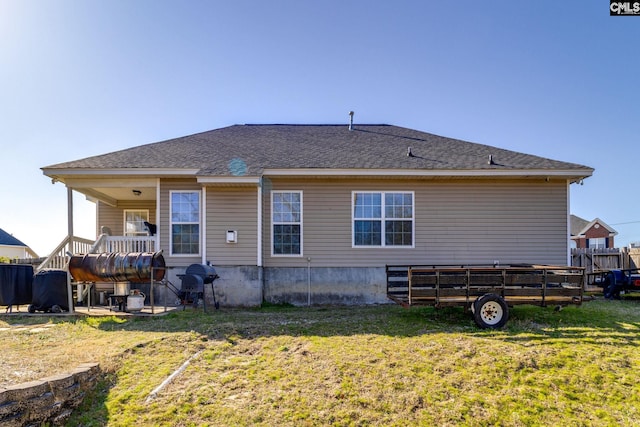 rear view of house with roof with shingles, a lawn, and fence